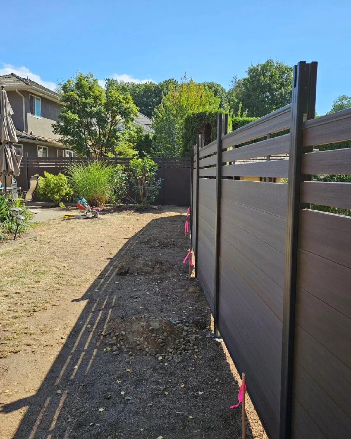 Dark composite privacy fence with horizontal slats along a backyard